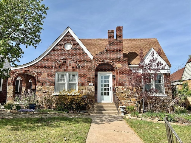 1909 N Gatewood Ave, Oklahoma City, OK 73106 - tudor home featuring roof with shingles, a chimney, stone siding, and brick siding