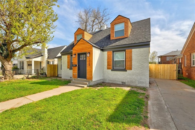 view of front of house with roof with shingles, fence, entry steps, a front lawn, and brick siding
