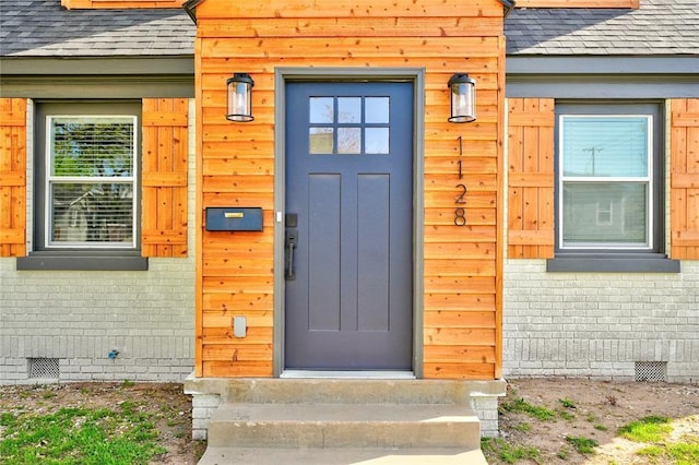 doorway to property with crawl space, brick siding, and roof with shingles