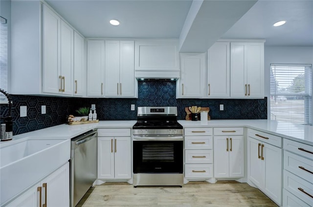 kitchen with light countertops, tasteful backsplash, appliances with stainless steel finishes, light wood-style flooring, and white cabinets