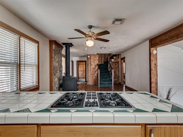 27704 S County Line Ave, Blanchard, OK 73010 - kitchen featuring a ceiling fan, tile counters, wood finished floors, a wood stove, and visible vents