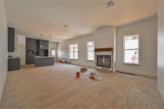 128 E 7th St, Arcadia, OK 73007 - unfurnished living room featuring visible vents, baseboards, a glass covered fireplace, and light wood-style floors