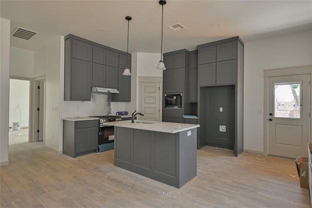 128 E 7th St, Arcadia, OK 73007 - kitchen featuring visible vents, a sink, under cabinet range hood, stainless steel gas stove, and gray cabinets