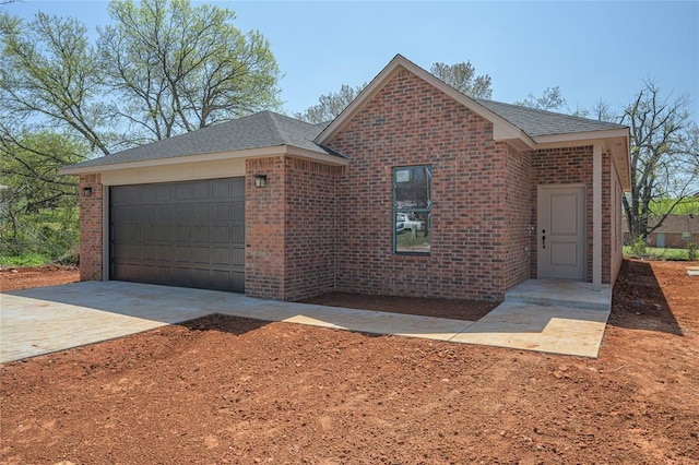 128 E 7th St, Arcadia, OK 73007 - view of front facade featuring concrete driveway, roof with shingles, brick siding, and an attached garage