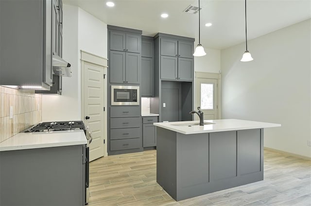 128 E 7th St, Arcadia, OK 73007 - kitchen featuring gray cabinetry, stainless steel appliances, a sink, light wood-type flooring, and a center island with sink