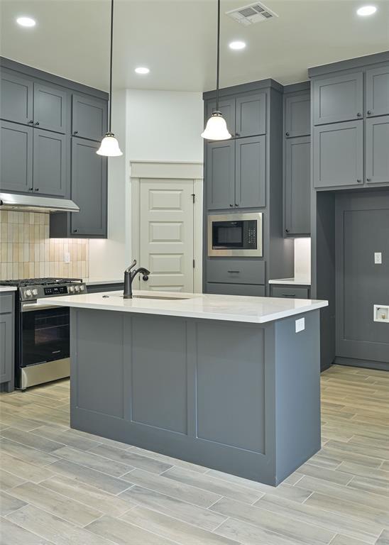 128 E 7th St, Arcadia, OK 73007 - kitchen with stainless steel appliances, a sink, light wood-style floors, light countertops, and an island with sink