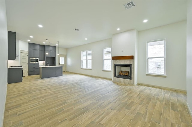 128 E 7th St, Arcadia, OK 73007 - kitchen featuring open floor plan, stainless steel microwave, a kitchen island with sink, light wood finished floors, and light countertops