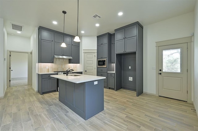128 E 7th St, Arcadia, OK 73007 - kitchen featuring stainless steel microwave, gray cabinets, under cabinet range hood, decorative backsplash, and light countertops