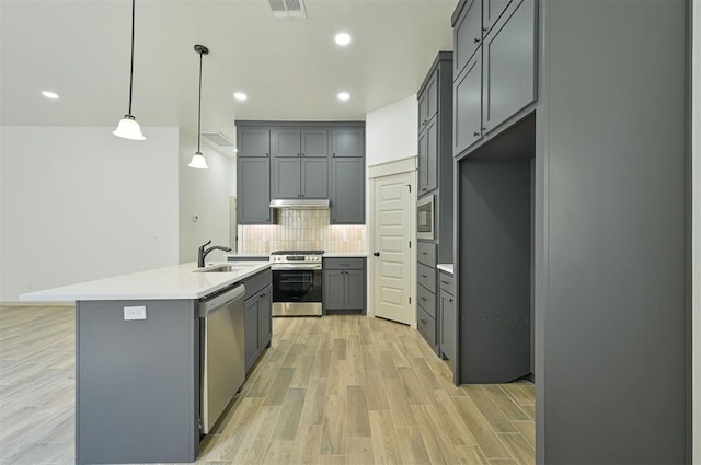 128 E 7th St, Arcadia, OK 73007 - kitchen with appliances with stainless steel finishes, gray cabinetry, under cabinet range hood, decorative backsplash, and a kitchen island with sink
