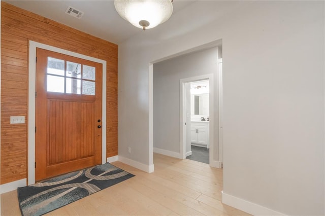 foyer with light wood-style flooring, wood walls, baseboards, and visible vents