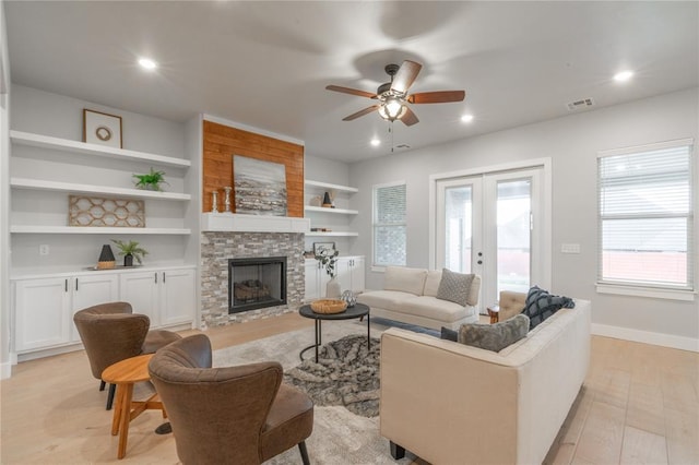 living area featuring a stone fireplace, baseboards, visible vents, light wood-style floors, and ceiling fan