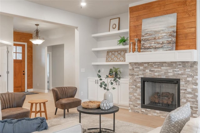 living area featuring baseboards, light wood-type flooring, built in features, and a fireplace