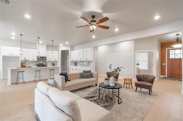 living area featuring a ceiling fan, light wood finished floors, wooden walls, visible vents, and recessed lighting