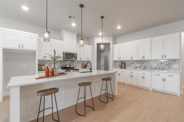 kitchen with stove, stainless steel microwave, light wood-style floors, visible vents, and white cabinets