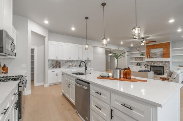 kitchen featuring white cabinetry, a sink, a ceiling fan, appliances with stainless steel finishes, and a fireplace