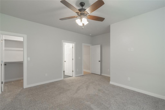 unfurnished bedroom with a spacious closet, carpet, baseboards, and ceiling fan
