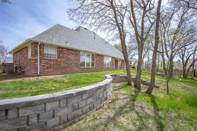 view of side of property with roof with shingles, a yard, and brick siding