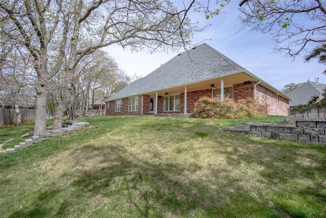rear view of property with a yard, a ceiling fan, fence, brick siding, and a shingled roof