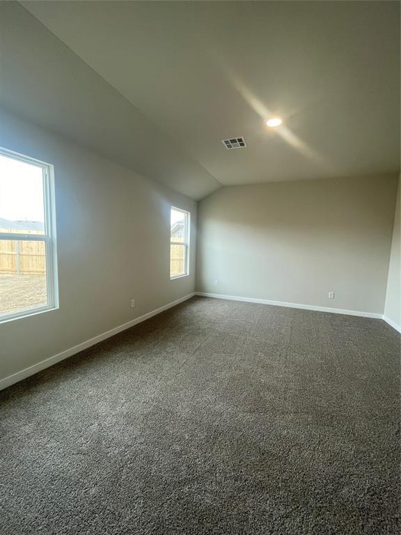 empty room featuring dark carpet, baseboards, vaulted ceiling, and visible vents