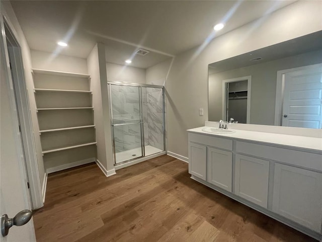 bathroom featuring vanity, a walk in closet, recessed lighting, a shower stall, and wood finished floors