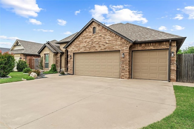 11609 SW 14th St, Yukon, OK 73099 - french country home featuring brick siding, an attached garage, concrete driveway, and roof with shingles