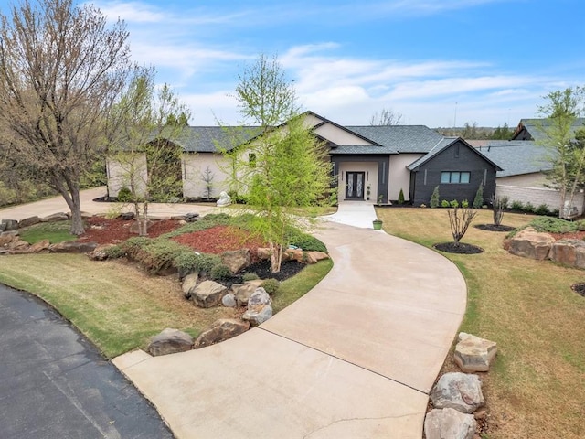 ranch-style house with curved driveway, a shingled roof, stucco siding, and a front lawn