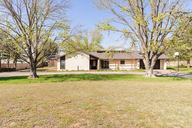 view of front of house featuring a front yard, fence, metal roof, and driveway