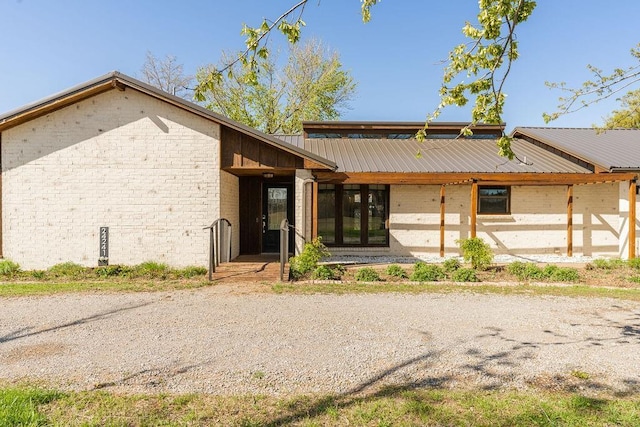 rear view of house featuring metal roof and brick siding