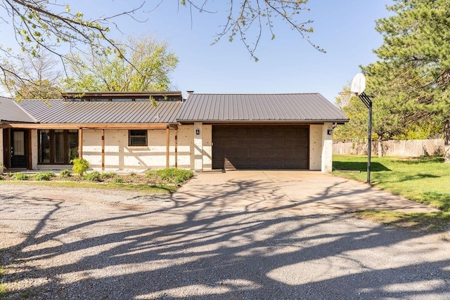 view of front facade with an attached garage, metal roof, driveway, and a front lawn