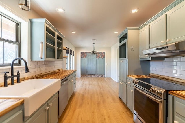 kitchen with butcher block counters, under cabinet range hood, a sink, and stainless steel appliances