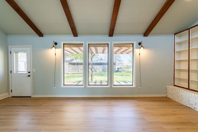 unfurnished living room featuring beamed ceiling, baseboards, plenty of natural light, and wood finished floors
