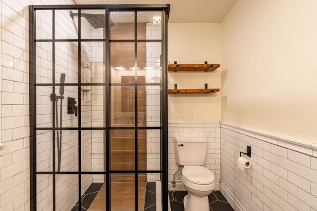 full bathroom with tiled shower, a wainscoted wall, tile walls, and toilet