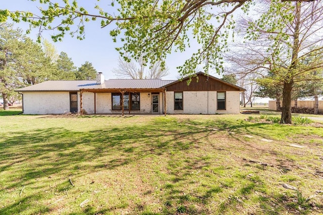 back of property featuring metal roof, a lawn, and a chimney