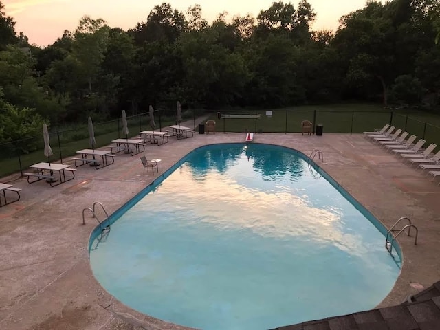 11230 Folkstone Dr, Yukon, OK 73099 - pool at dusk featuring a patio area, a community pool, fence, and view of wooded area
