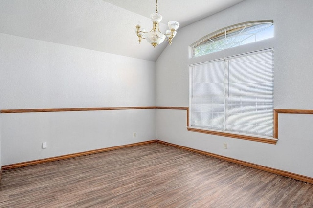 empty room with a chandelier, baseboards, vaulted ceiling, and wood finished floors