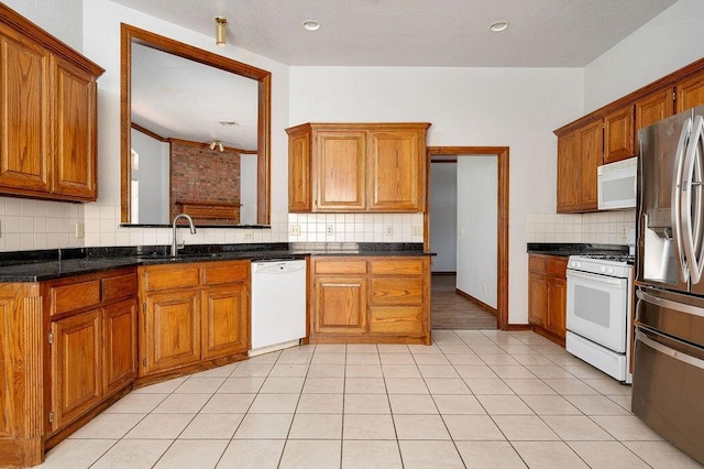 kitchen with light tile patterned floors, a sink, white appliances, brown cabinets, and decorative backsplash