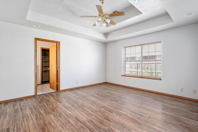 unfurnished room featuring a textured ceiling, wood finished floors, a ceiling fan, and a raised ceiling