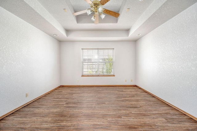 empty room featuring a tray ceiling, wood finished floors, a textured wall, and baseboards
