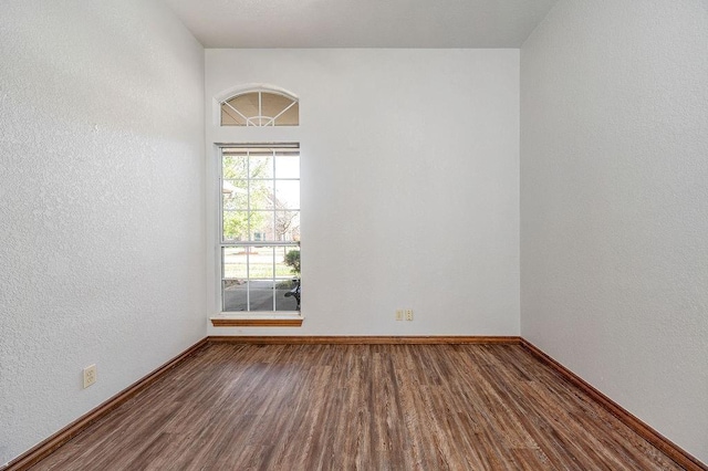 spare room featuring a textured wall, baseboards, and wood finished floors