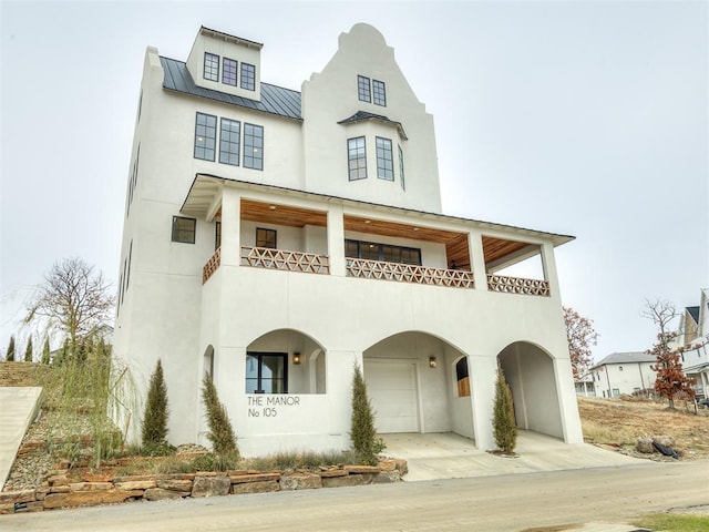 view of front of property with an attached garage, a balcony, a standing seam roof, and stucco siding