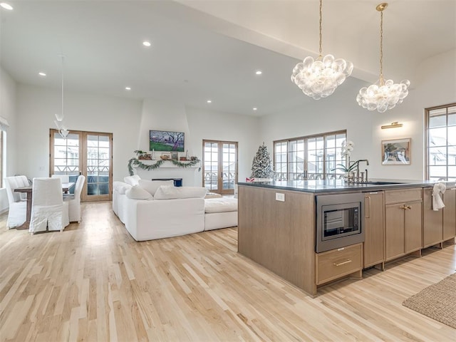kitchen with light brown cabinetry, a sink, stainless steel microwave, open floor plan, and light wood-style floors