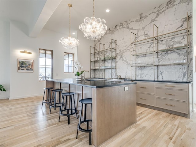 kitchen with a breakfast bar area, dark countertops, a kitchen island with sink, and light wood-type flooring