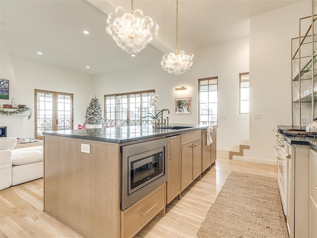 kitchen featuring a center island, a sink, stainless steel microwave, a chandelier, and light brown cabinets