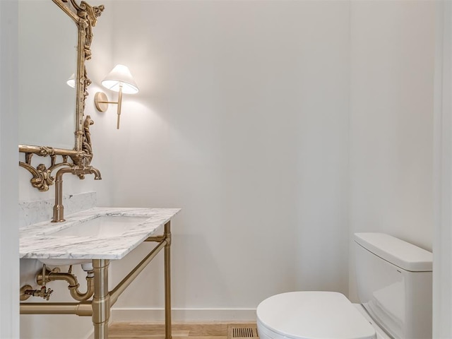 half bath featuring wood finished floors, baseboards, a sink, and toilet