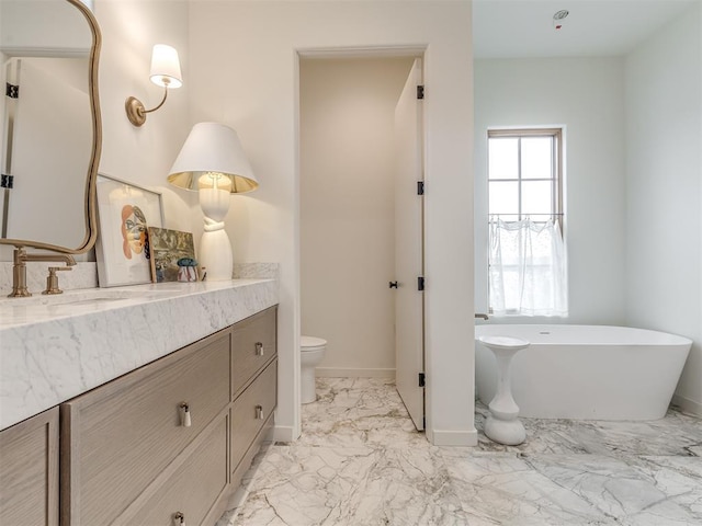 bathroom featuring vanity, marble finish floor, a soaking tub, baseboards, and toilet