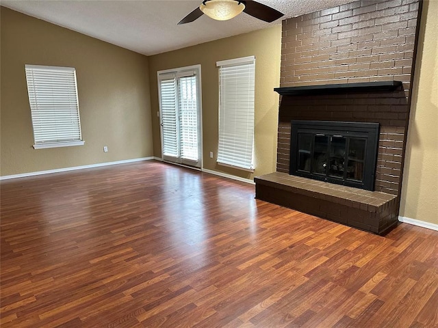 unfurnished living room with lofted ceiling, baseboards, ceiling fan, a brick fireplace, and wood finished floors