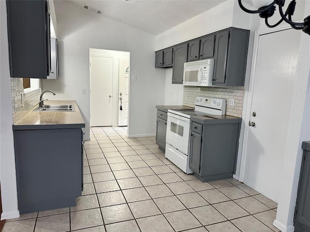 kitchen with a sink, lofted ceiling, light tile patterned floors, white appliances, and visible vents