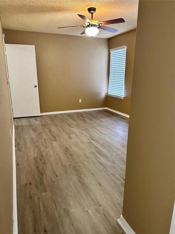 empty room featuring a textured ceiling, wood finished floors, baseboards, and a ceiling fan