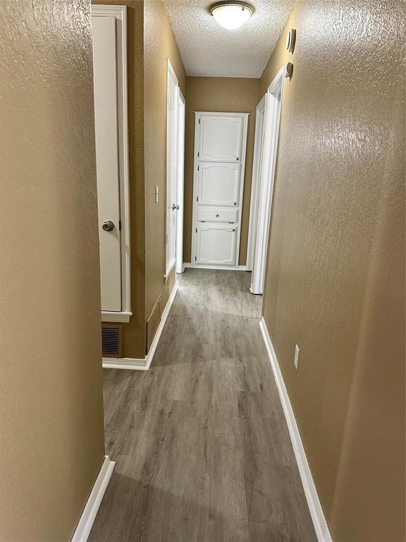 corridor with baseboards, visible vents, a textured ceiling, and wood finished floors