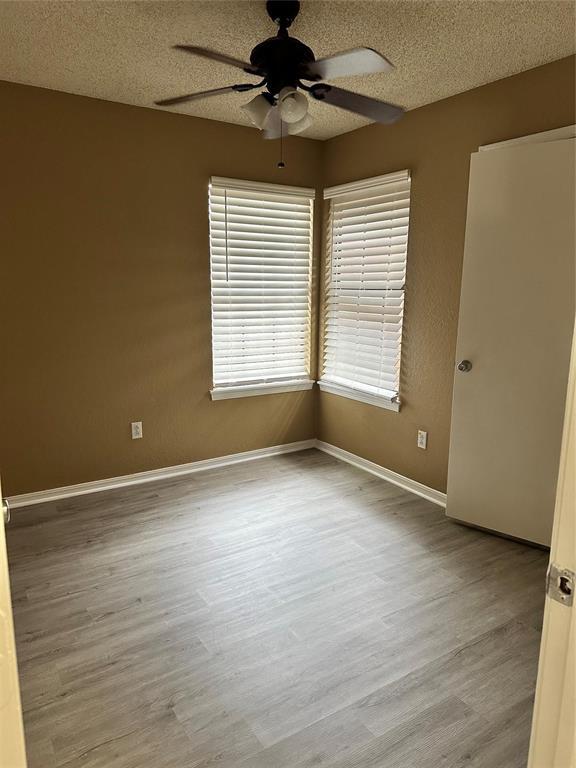 unfurnished room featuring baseboards, a textured ceiling, wood finished floors, and a ceiling fan